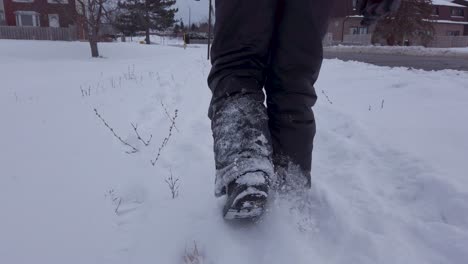 Kleines-Kind,-Das-Im-Winter-Mit-Grauen-Schneehosen,-Stiefeln-Und-Handschuhen-Im-Schnee-Entlang-Der-Straße-Läuft