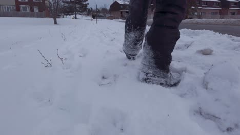 Young-child-walking-in-snow-on-side-of-road-in-winter-wearing-grey-snowpants-and-snow-boots