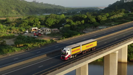 Aerial-tracking-shot-of-yellow-transport-truck-crossing-a-highway-bridge