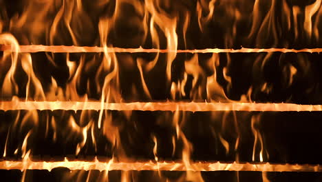 Picturesque-scene-of-red,-orange-and-yellow-vertical-hot-flames-burning-horizontal-wood-logs-of-home-with-fire-raging-in-background,-static-close-up