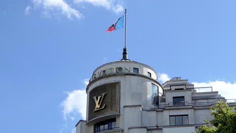 Louis-Vuitton-Flag-waving-in-the-wind-on-the-roof-of-the-Parisian-boutique-Store-on-the-Champs-Elysées,-Paris,-France