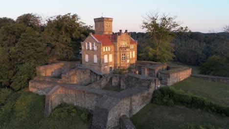 Close-aerial-drone-orbit-of-restored-medieval-castle-on-ridge-lit-up-by-golden-dawn