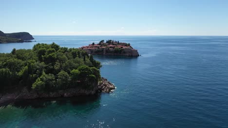 Drone-flying-over-trees-and-sea,-focusing-on-Sveti-Stefan-peninsula