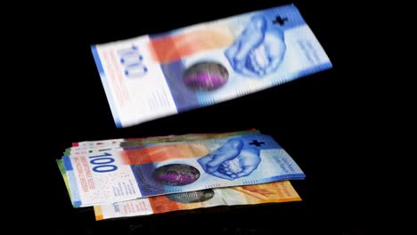 Swiss-franc-bills-are-slowly-raining-down-from-above-forming-a-pile-against-a-black-background