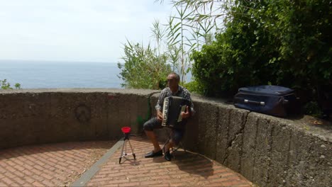 Street-musician-with-an-accordion-plays-and-sings-songs-on-the-cinque-terre-trails-in-Italy,-Elderly-man-plays-the-accordion