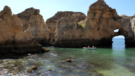 Boat-Under-Rock-Formations-and-Natural-Arch-of-Ponta-de-Piedade,-Alragve,-Portugal,-Pan-Left-50fps