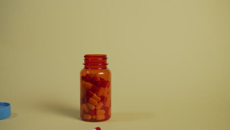 Slow-motion-wide-shot-of-a-bottle-of-pills-falling-and-landing,-the-lid-pops-off-and-a-single-pill-bounces-out