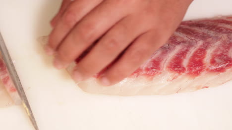 Chef-Cutting-Meat-Of-Fresh-Raw-Fish-In-Slow-Motion-For-Sushi-Making-In-A-Japanese-Restaurant---high-angle-shot,-close-up