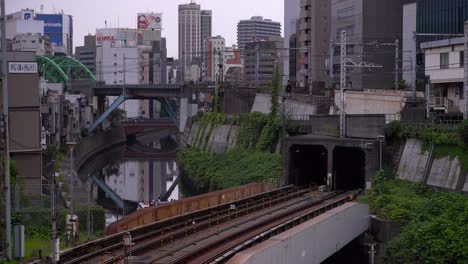 Un-Barco-Turístico-Navegando-Por-El-Río-Bajo-El-Ferrocarril-En-Tokio,-Japón,-Con-Edificios-De-Gran-Altura-Al-Fondo---Plano-Amplio