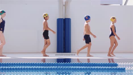 Kinder-Laufen-In-Aufsteigender-Altersreihenfolge-Von-Links-Nach-Rechts-Am-Beckenrand-Entlang-–-Schwimmkurs-–-Totale