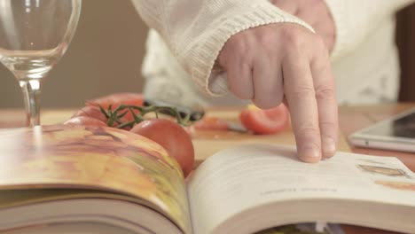 Hands-cutting-fresh-vine-tomatoes-in-kitchen-with-recipe-book-close-up-shot