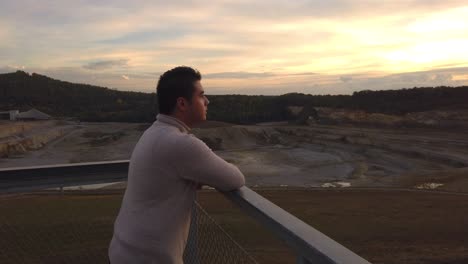 A-young-man-in-an-turtleneck-sweater-looking-over-the-quarry-while-the-sun-is-setting