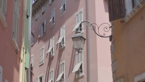 Slowmotion-shot-of-an-old-lantnern-lamp-in-an-alleyway-in-Riva-Del-Garda-with-a-rosa-italian-building-in-the-background