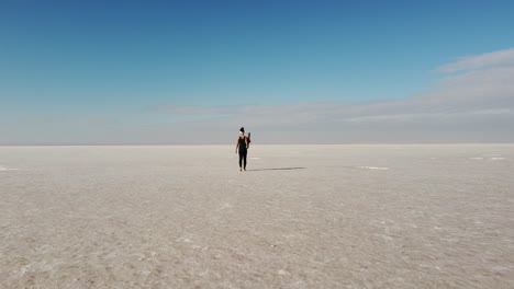 Beautiful-young-woman-walking-with-a-yoga-mat-in-the-middle-of-a-salt-flat