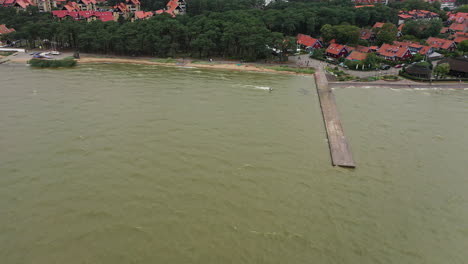 AERIAL:-Wide-Shot-of-Kite-Surfer-Jumping-Over-Stone-Pier