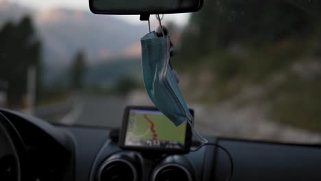 Face-mask-hanging-on-drivers-rear-mirror-while-car-moving-on-road-Covid-19-virus-pandemic-outbreak,-detail-slow-motion