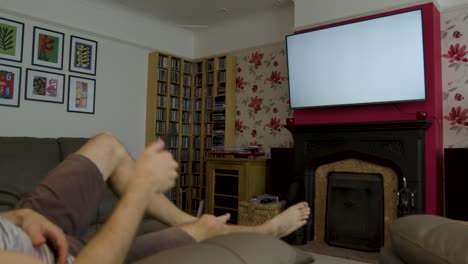 Male-lazily-reclining-on-a-sofa-using-a-TV-remote-on-a-white-screen-TV