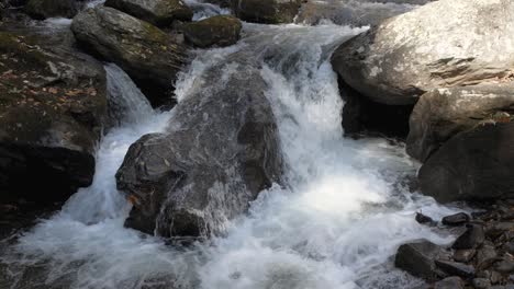 Mountain-stream-splashes-over-river-rocks-in-small-waterfall,-slow-motion