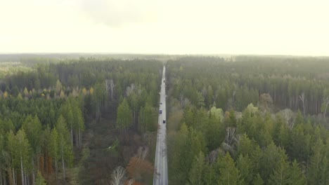 Pullback-shot-of-a-drone-over-a-autumn-colored-forest-tracking-a-transporter-car-while-flying-backwards-with-the-copter