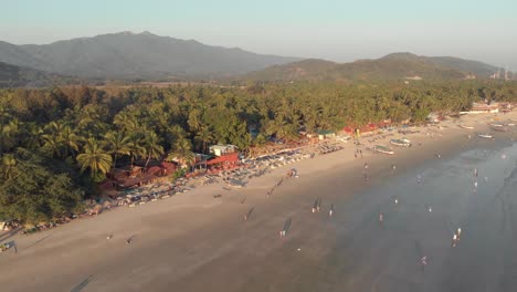 People-stroll-along-Palolem-beach-sand-and-calming-sea-waves,-Goa,-India