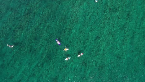 Young-surfers-catching-waves-in-a-calm-beach-in-the-Maldives-islands,-Aerial-top-view-lowering-shot