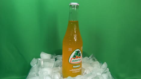 2-2-Kohlensäurehaltige-Mango-Getränkeflaschen,-Die-Sich-Um-360-Grad-Drehen,-Auf-Gestapeltem-Eis-Vor-Einem-Grünen-Bildschirm