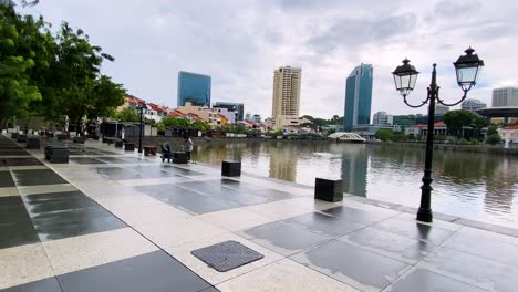 Worker-Picking-Up-Trash-On-Empty-Space-In-Front-Of-United-Overseas-Bank-Plaza-Facing-Singapore-River-During-The-Pandemic---Wide-Shot