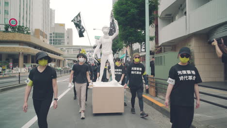 Lady-Liberty-Statue-On-A-Wooden-Cart-Symbolizing-Liberation-Of-Hong-Kong-Pushed-By-People-Wearing-Facemask-At-Solidarity-Protest-In-Tokyo,-Japan