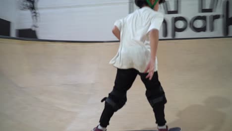 Young-male-kid-riding-skateboard-on-ramp-inside-lighting-indoor-skate-park