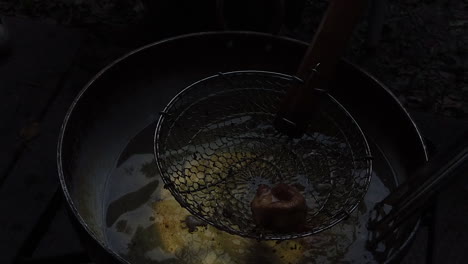 A-spider-strainer-retrieving-a-fried-dumpling-from-a-large-wok-of-hot-oil