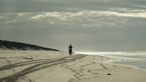 Biker-rides-on-motocross-motorcycle-on-sandy-beach-alongside-shiny-sea