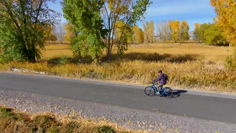 Senior-man-cycling-along-a-paved-nature-trail-in-autumn---aerial-view