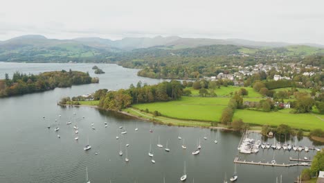 aerial-shot-from-a-drone-of-lake-windermere-in-the-foreground-there-are-fields-and-the-small-town-of-bowness-in-the-background-you-can-see-the-mountains-and-hills-of-the-Lake-District
