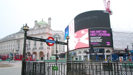 Lockdown-in-London,-red-buses-slow-mo-gimbal-shot-of-Piccadilly-Circus-underground-station-empty-in-front-of-LED-signage-announcing-corona-virus-messages