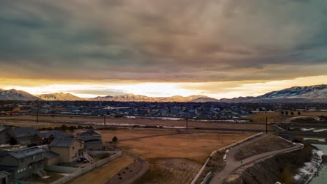 Gloomy-cloudscape-above-the-sunshine-with-an-urban-area-below-and-the-snow-mountains-in-the-distance---aerial-hyperlapse
