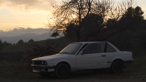 Man-drives-white-vintage-car-into-sunset-landscape,-parks,-and-gets-out