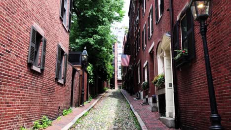 Boston-Beacon-Hill-Acorn-Street-neighborhood-with-brown-brick-federal-style-rowhouses-and-narrow-cobblestone-sidewalk,-gas-lanterns,-US-flag