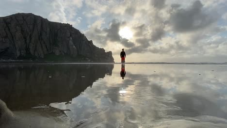 Freedom,-guy-walking-at-the-beach-in-morro-bay-california,-iconic-morro-bay-rock,-water-reflection