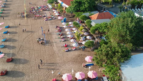 Aerial-flyover-beautiful-Legian-beach-with-sunshades-and-tourist-during-sunny-day