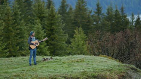 A-man-is-playing-the-guitar-at-the-top-of-a-mountain-surrounded-by-a-forest