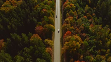 Autumn-colors:-Look-up-aerial-shot-from-following-a-driving-car-with-oncoming-traffic-at-a-sunny-day-in-fall,-up-to-the-bright-horizon-with-mountains-and-a-little-city-at-the-end-of-the-straight-road