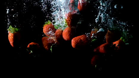 Strawberries-dropped-into-water-on-black-background,-slow-motion-close-up