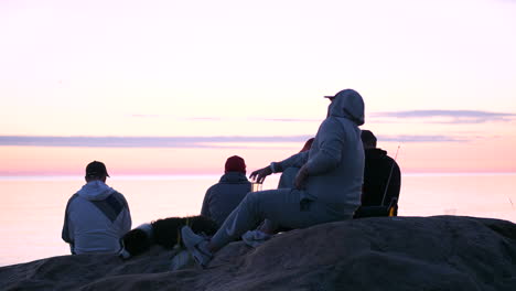 A-group-of-male-friends-sit-atop-a-rocky-landscape-watching-the-orange-sunset-glow