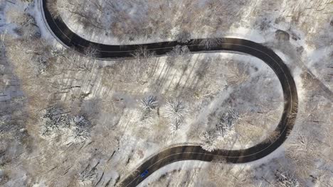Topdown-aerial-view-at-a-snowy-serpentine-road-with-driving-cars-from-both-sides---top-shot-at-the-wintertime-with-snow-covered-trees-surrounding-the-street
