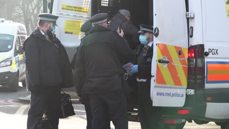 Police-officers-in-face-masks-escort-a-detained-man-retrained-in-handcuffs,-who-is-suspected-of-breaching-Coronavirus-legislation,-into-a-police-van