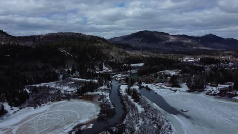 Aerial-drone-shot-of-landscape-with-water-stream-and-mountains-during-winter-in-Ste-Ã‰mÃ©lie-de-l'Ã‰nergie,-QuÃ©bec,-Canada
