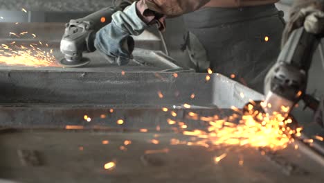 Two-Blacksmiths-grinding-metal-plates-with-circular-saw-in-metal-casting-factory,-closeup-slow-motion-shot-of-sparks-flying-from-hot-metal
