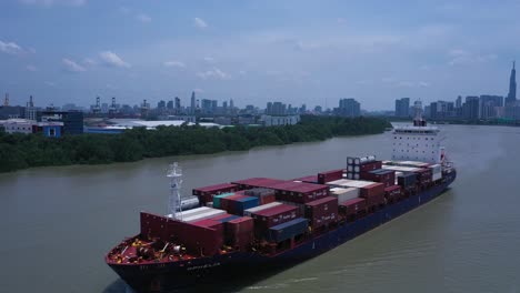 Aerial-panning-view-of-large-container-ship-passing-along-the-Saigon-river-in-Ho-Chi-Minh-City,-Vietnam-on-sunny-day-with-a-clear-blue-sky-and-low-air-pollution