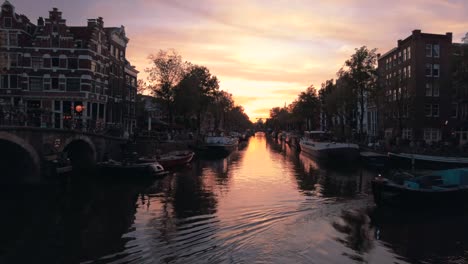 Timelapse-De-Una-Impresionante-Puesta-De-Sol-Naranja-Con-Un-Canal-Lleno-De-Barcos-En-Amsterdam