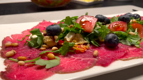 Static-close-up-of-delicious-served-dinner-with-fresh-raw-beef-with-salad,tomato,blueberry-and-pine-nuts
